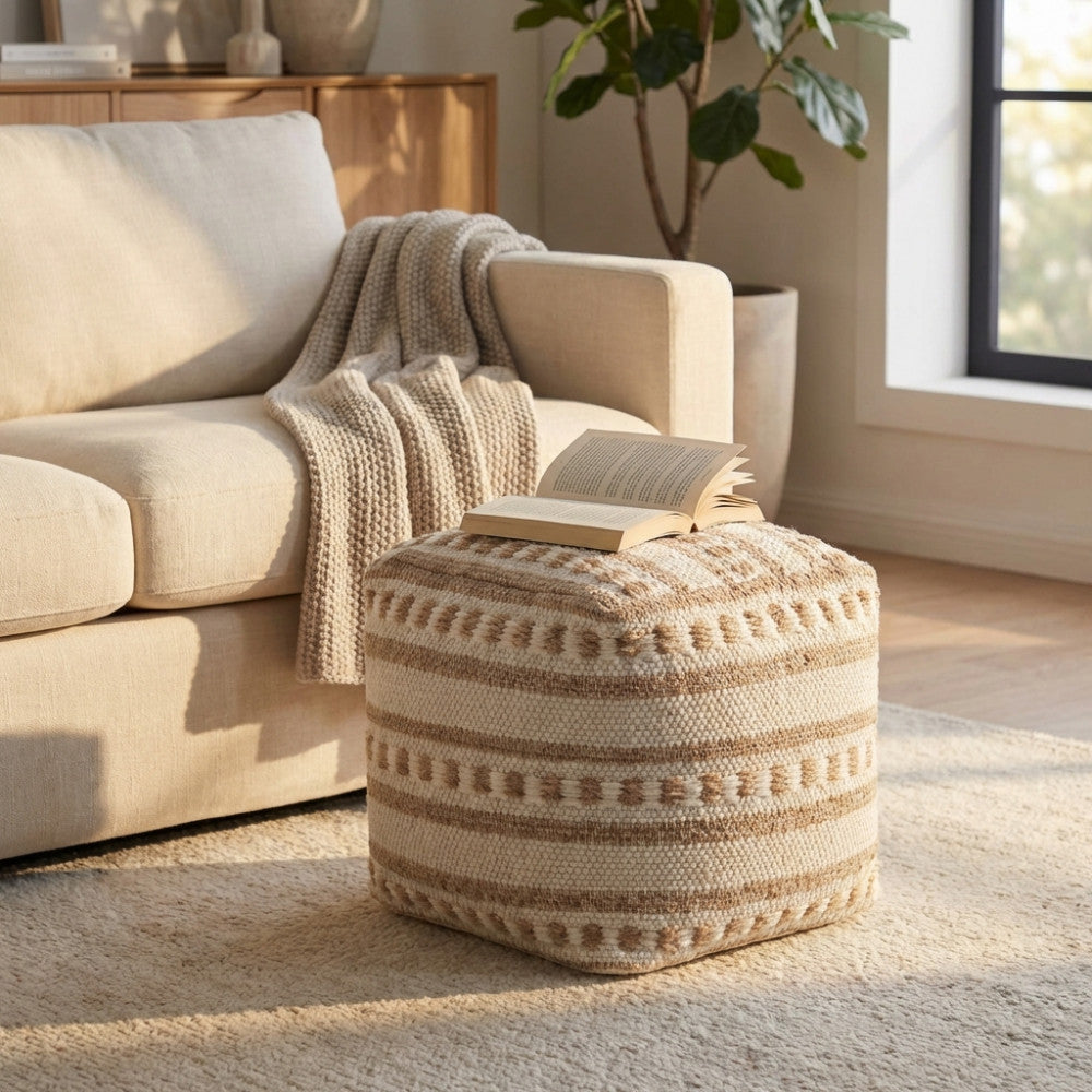 Pouf quadrato Nicolas in cotone e lana bianco e marrone chiaro, ambientato in un soggiorno luminoso accanto a un divano beige con un libro aperto sopra.