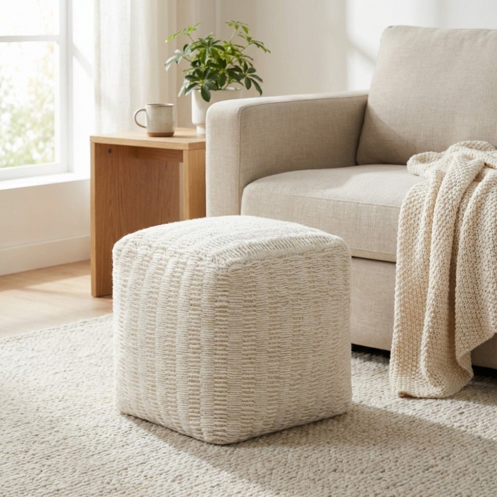 Pouf Renaud in lana e cotone bianco posizionato su un tappeto chiaro in un salotto moderno e luminoso.