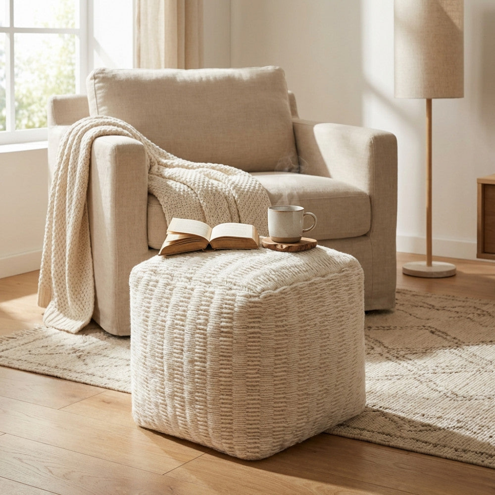 Dettaglio del pouf Renaud bianco utilizzato come piano d'appoggio per un libro e una tazza in un ambiente living elegante.
