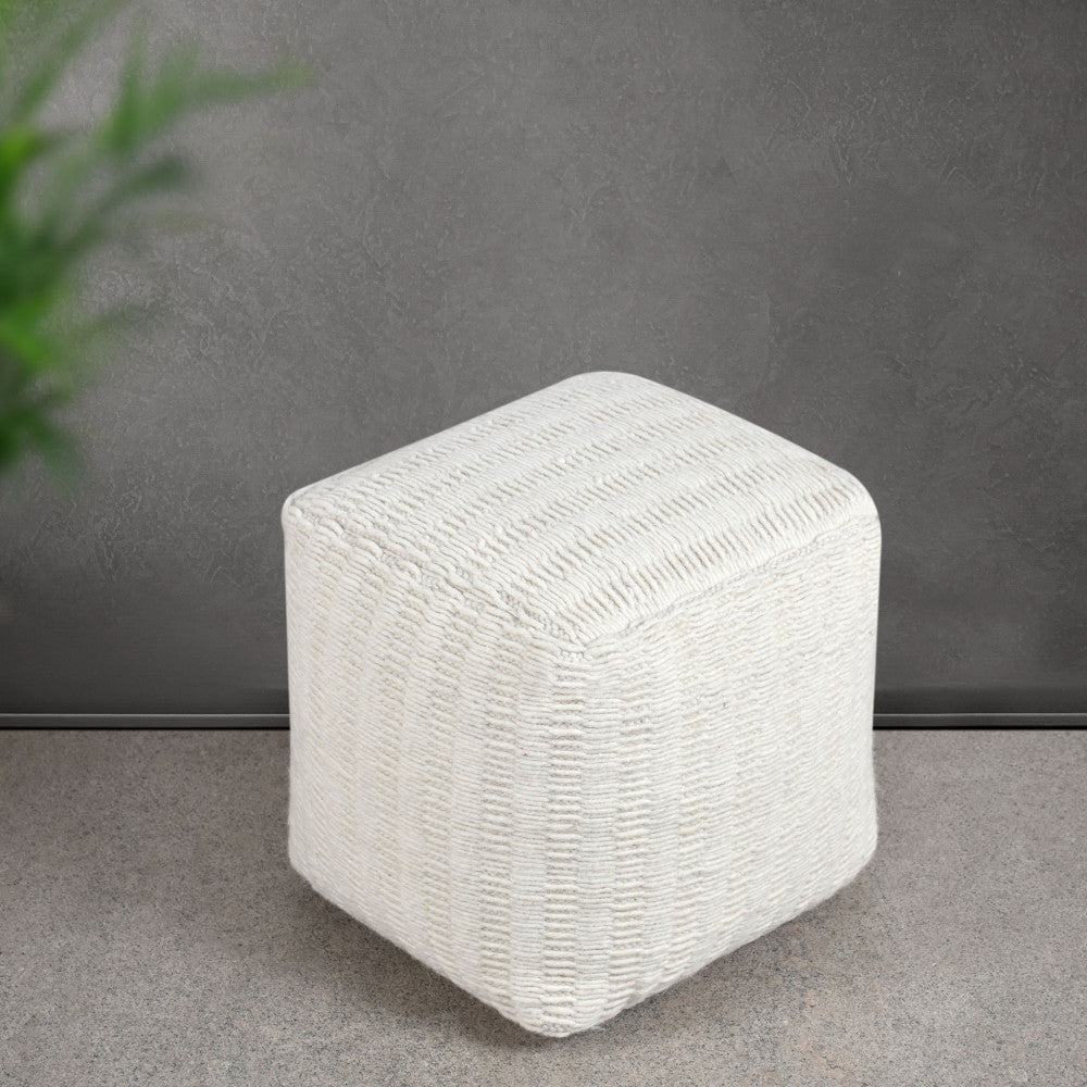 Pouf moderno Renaud in tessuto bianco a contrasto su un pavimento in pietra grigia e parete scura.
