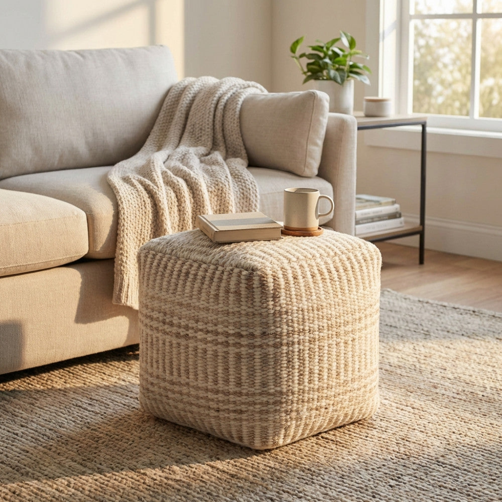 Pouf Roméo in lana e cotone bianco ecrù, utilizzato come tavolino da salotto con un libro e una tazza, accanto a un divano chiaro.