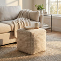 Pouf Roméo in lana e cotone bianco ecrù, utilizzato come tavolino da salotto con un libro e una tazza, accanto a un divano chiaro.
