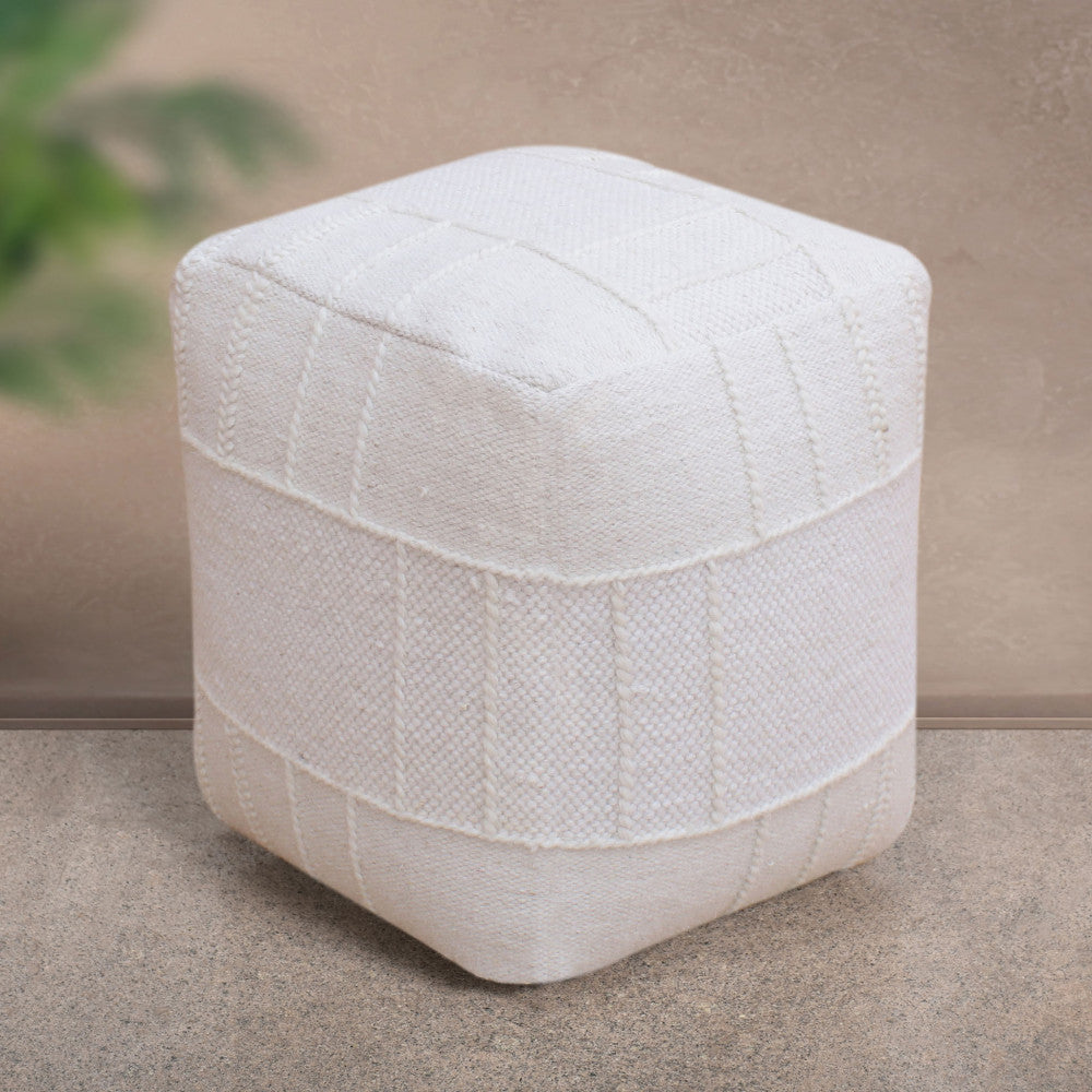 Pouf moderno bianco in lana e cotone ambientato su un pavimento in pietra neutra, con una pianta sfocata sullo sfondo.