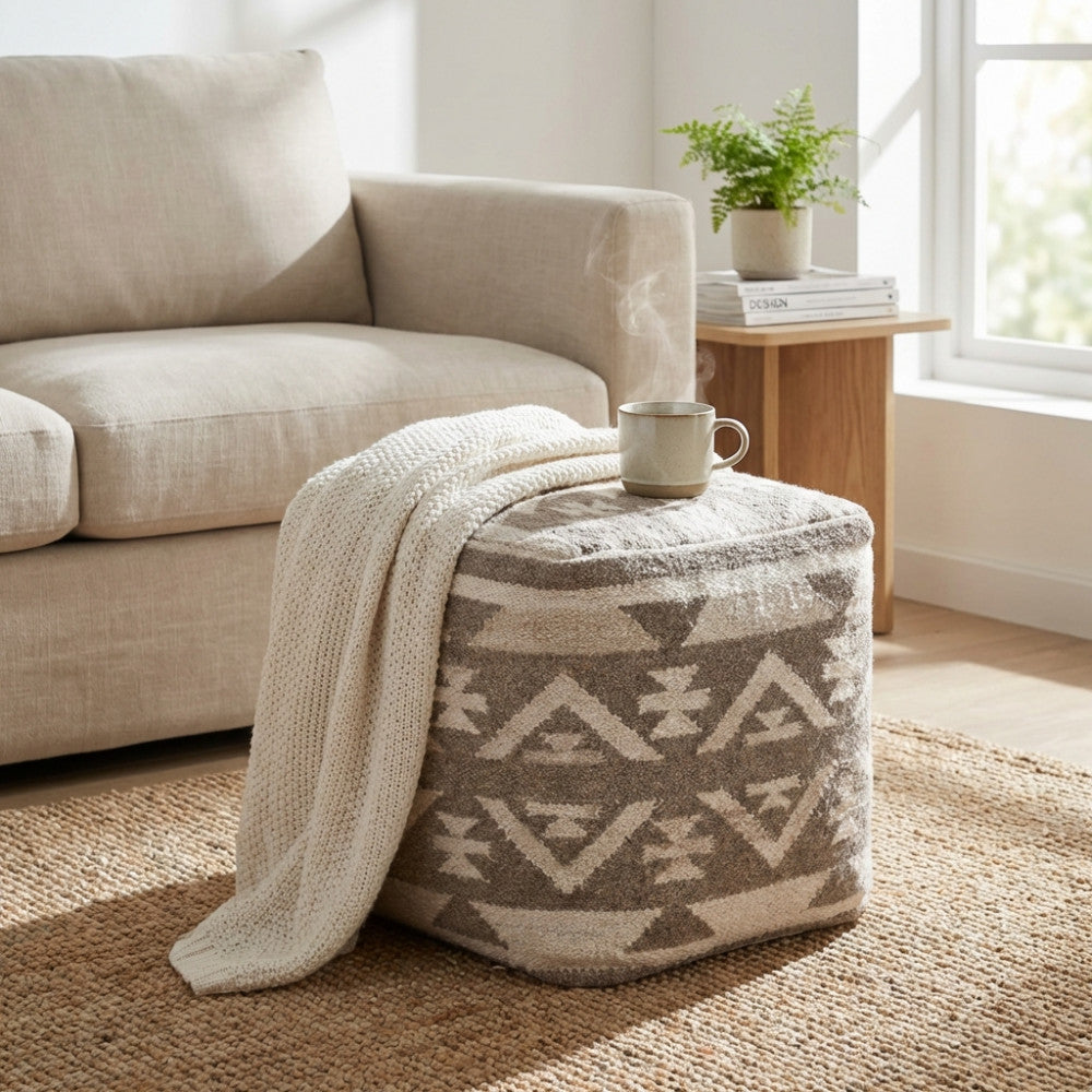 Dettaglio del Pouf Romaric con coperta in maglia appoggiata, posizionato accanto a un divano beige in un ambiente accogliente.