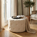 Pouf rotondo in velluto beige posizionato in un salotto luminoso con vassoio e tazza di caffè.