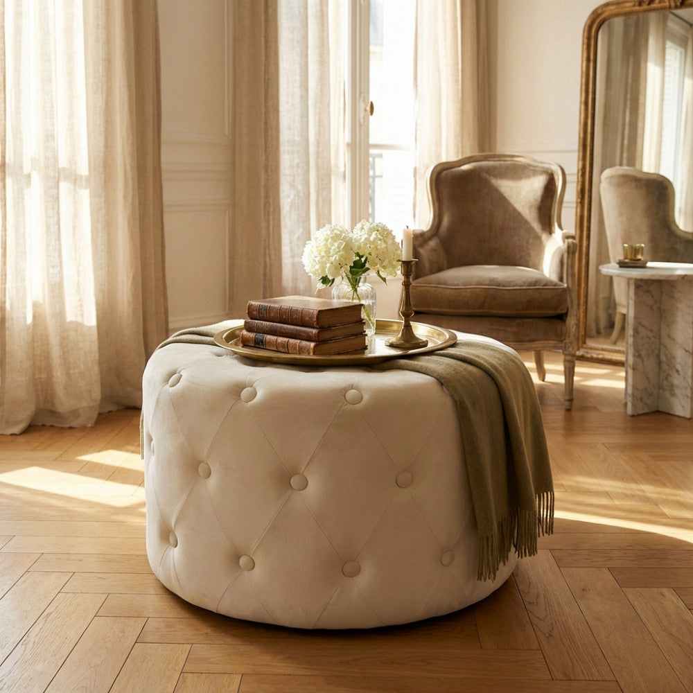 Pouf rotondo in velluto beige utilizzato come tavolino centrale con libri antichi e vassoio dorato.