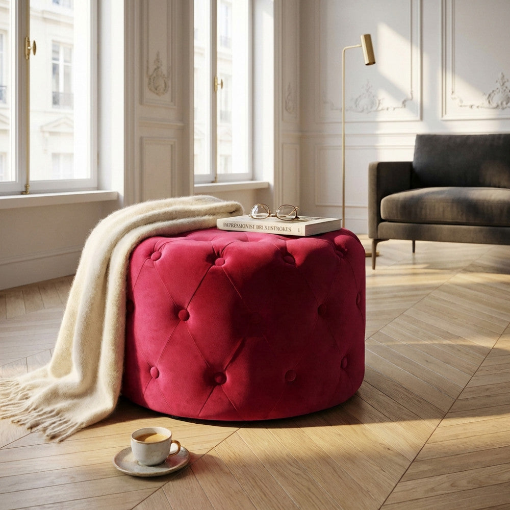 Dettaglio del pouf capitonné rosso scuro illuminato dalla luce naturale in un ambiente classico con pavimenti in parquet a spina di pesce.