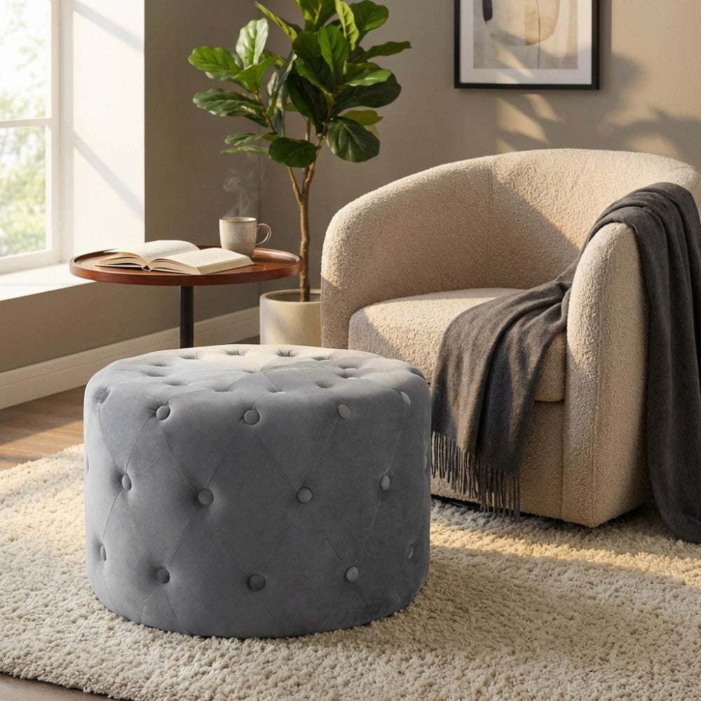 Pouf rotondo in velluto grigio scuro posizionato su un tappeto chiaro in un salotto luminoso.
