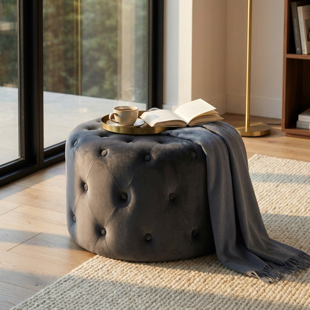 Pouf capitonnè grigio scuro utilizzato come tavolino con un vassoio dorato, tazza e libro.