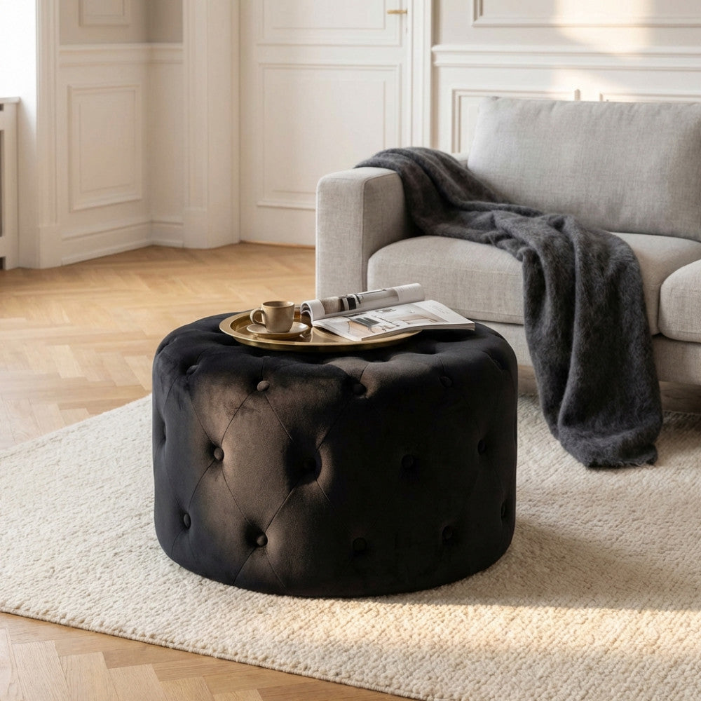 Dettaglio del pouf rotondo in velluto nero illuminato dalla luce naturale in un elegante soggiorno contemporaneo.