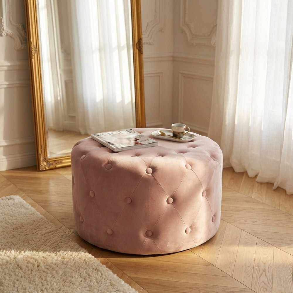 Pouf rotondo in velluto rosa con lavorazione capitonné situato in un elegante salotto con specchio dorato e parquet.