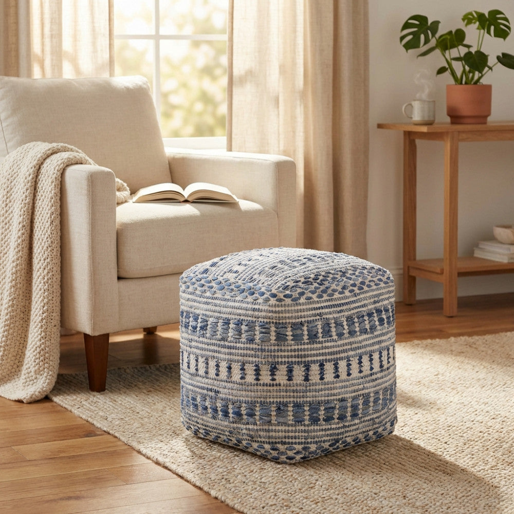 Dettaglio del pouf Sébastien accanto a una poltrona beige, che mostra la texture intrecciata in lana e cotone illuminata dalla luce naturale della finestra.