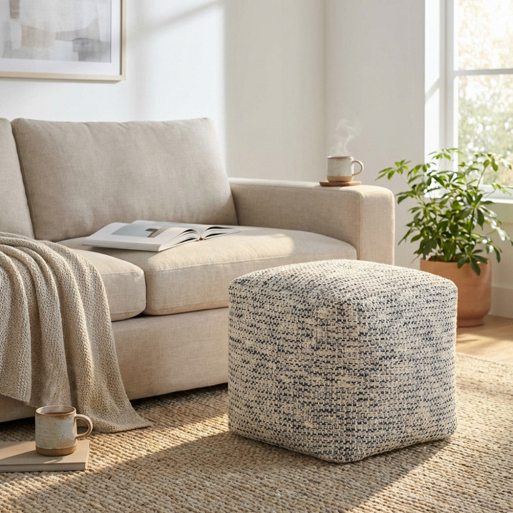 Pouf Samuel in cotone blu melange e bianco, posizionato su un tappeto in juta accanto a un divano beige in un luminoso soggiorno moderno.