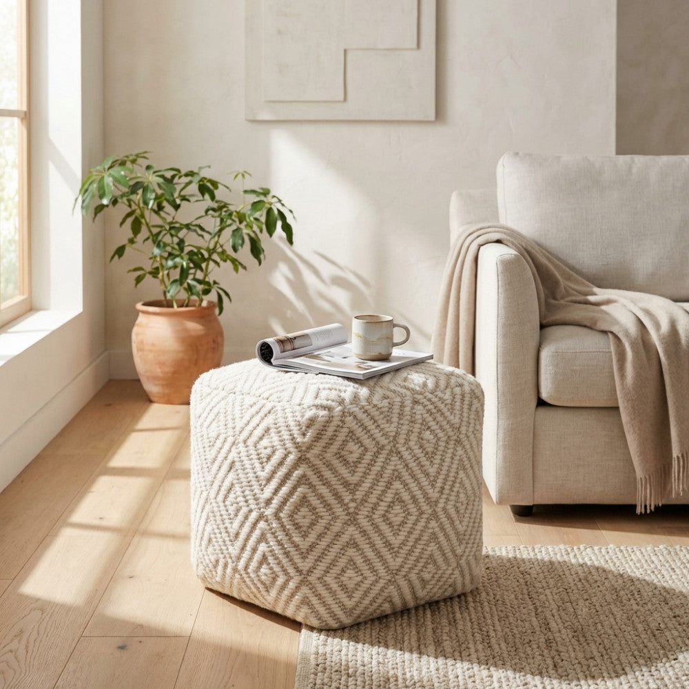 Pouf Simeon in lana bianca e marrone chiaro posizionato in un luminoso soggiorno moderno accanto a un divano beige.