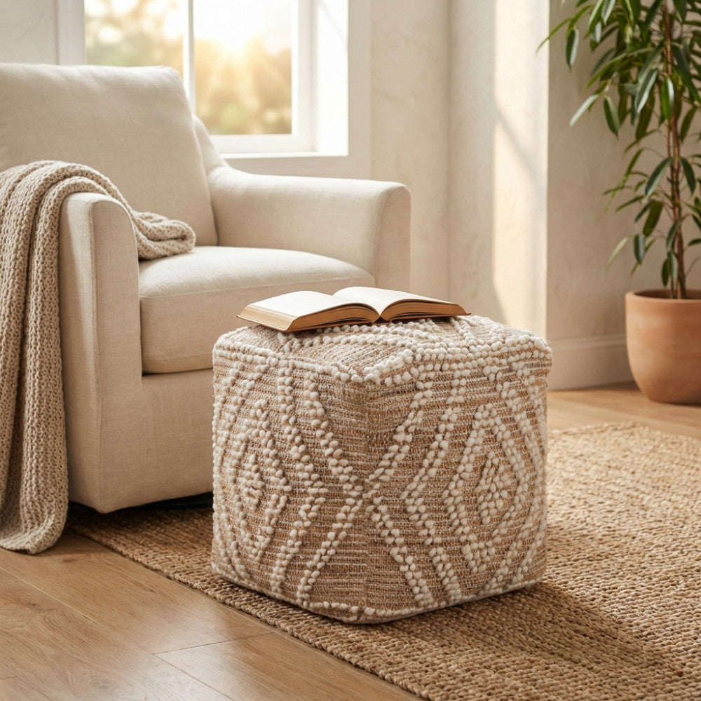Pouf Térence quadrato in juta e lana ecrù posizionato su un tappeto in fibra naturale accanto a una poltrona chiara.