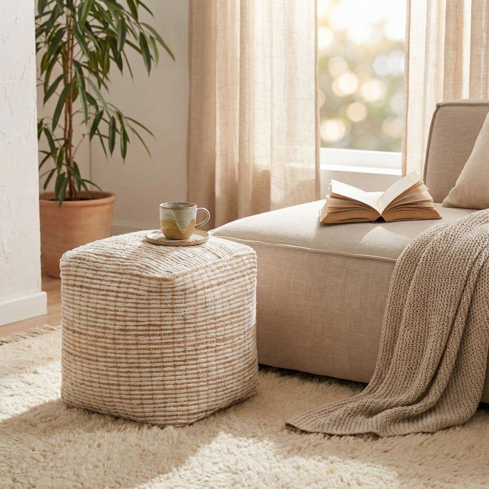 Pouf Théo in juta e lana posizionato accanto a un divano chiaro, con tazza e libro appoggiati, illuminato da luce naturale.