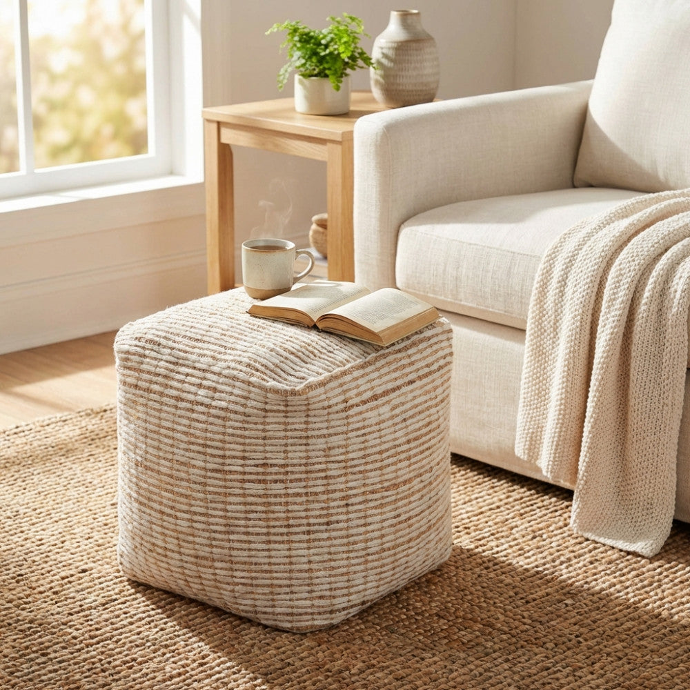 Dettaglio del pouf Théo su un tappeto in fibre naturali, utilizzato come tavolino d'appoggio per una bevanda calda e un libro aperto.