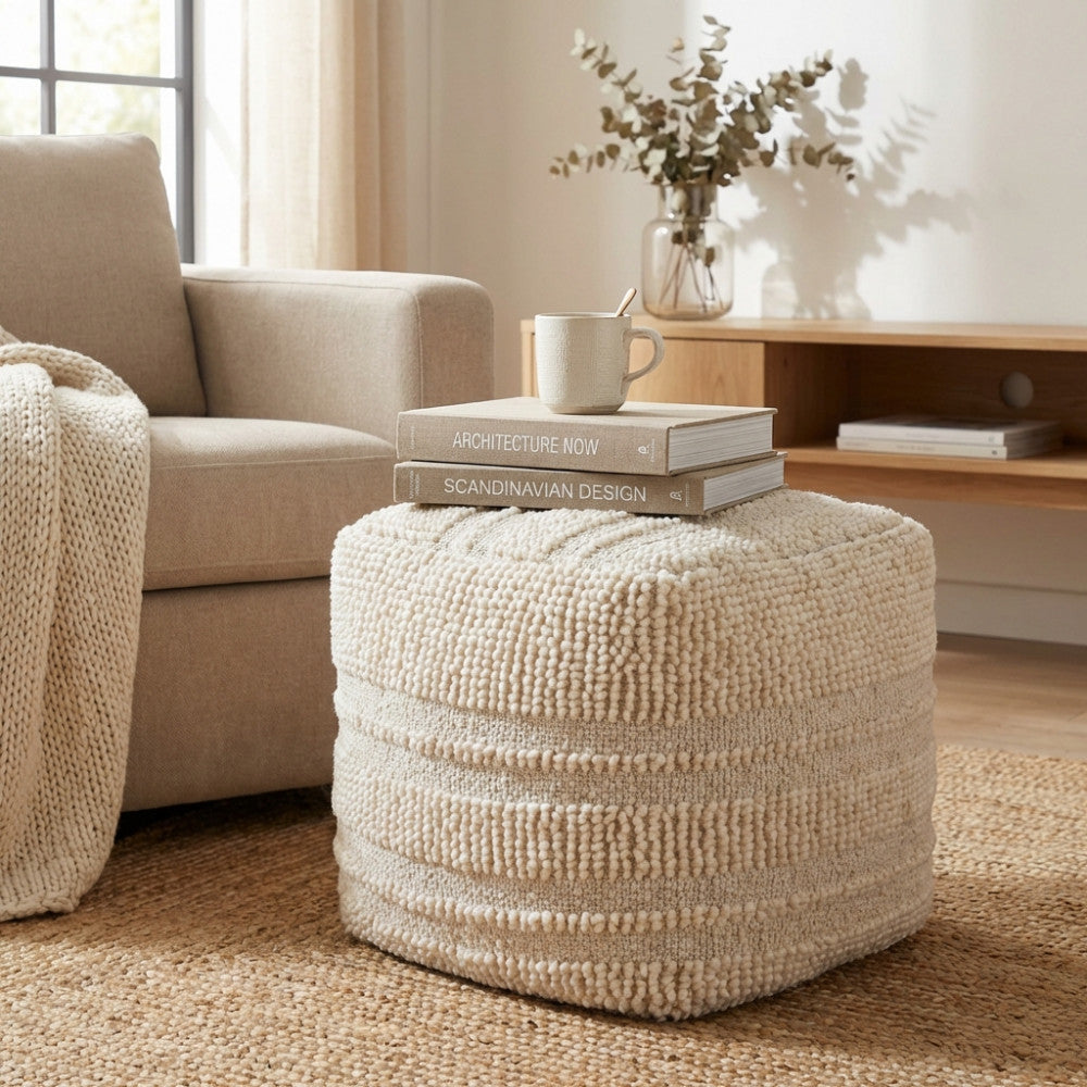 Pouf Théotime in lana bianca ambientato in un salotto luminoso con libri di design appoggiati sulla superficie.