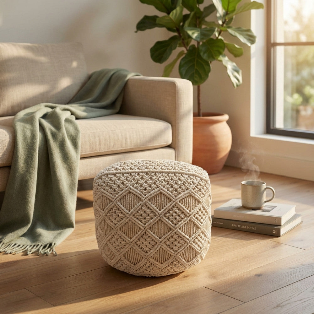Pouf Tripoli intrecciato a mano posizionato su un pavimento in parquet vicino a un divano elegante.