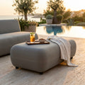 Pouf modulare Tucumán grigio scuro ambientato a bordo piscina al tramonto con vassoio e drink.