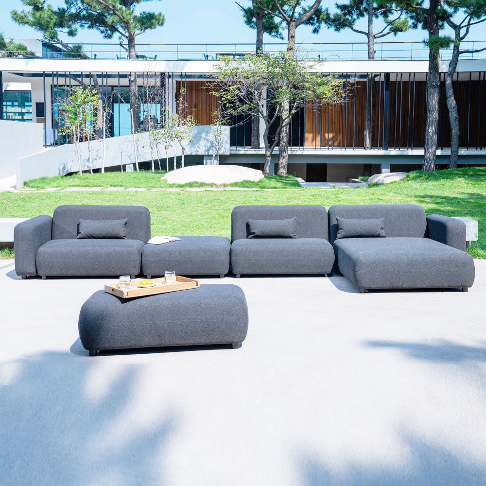 Set lounge completo da esterno con il pouf Tucumán integrato in un ampio giardino dal design contemporaneo.