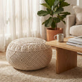 Pouf Zoumi in cotone bianco intrecciato, posizionato su un tappeto testurizzato accanto a un tavolino in legno chiaro in un luminoso soggiorno boho.
