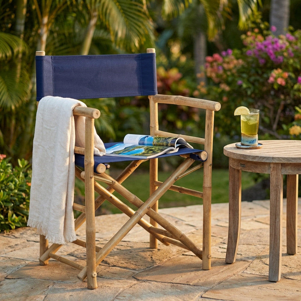 Poltroncina pieghevole in bamboo e tessuto blu posizionata su un pavimento in pietra tra piante tropicali.