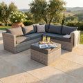 Salotto angolare in wicker grigio con cuscini sfoderabili ambientato in un giardino lussuoso al tramonto.