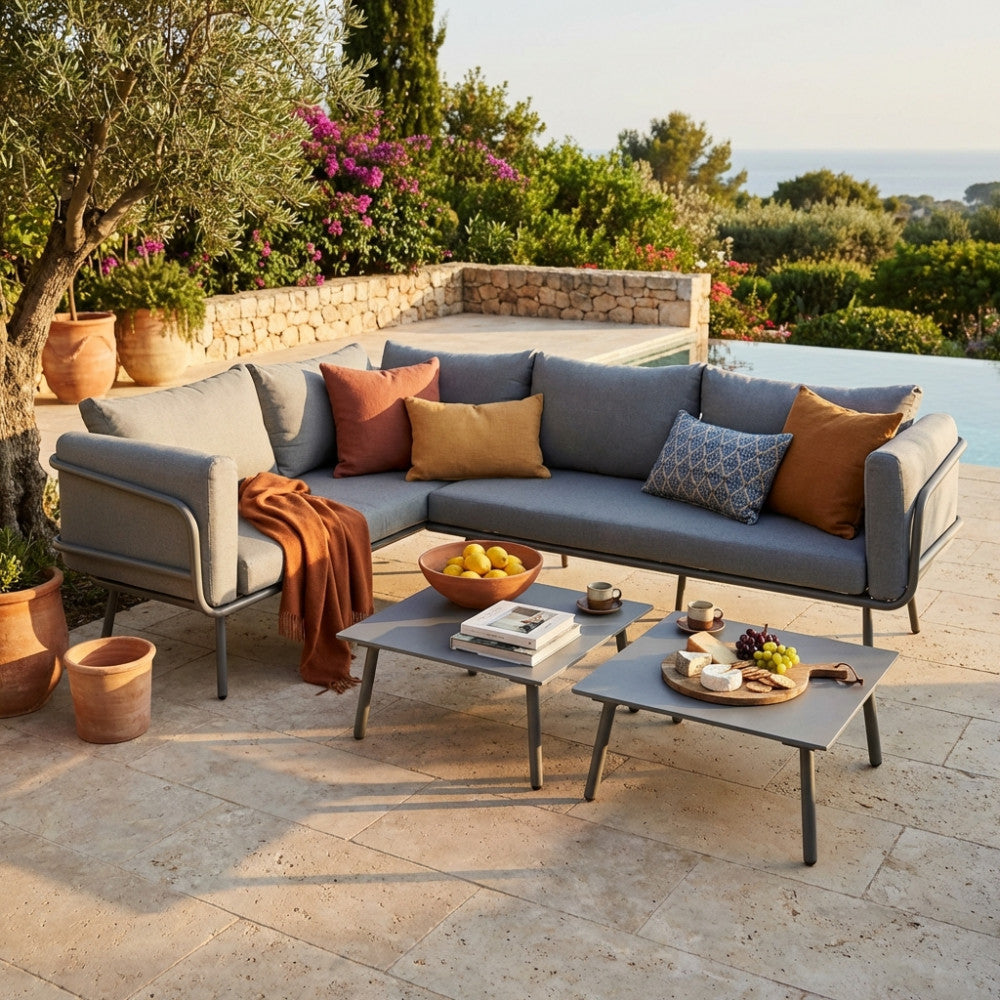 Salotto angolare Suez in alluminio grigio a sei posti, allestito a bordo piscina con cuscini decorativi e due tavolini bassi.