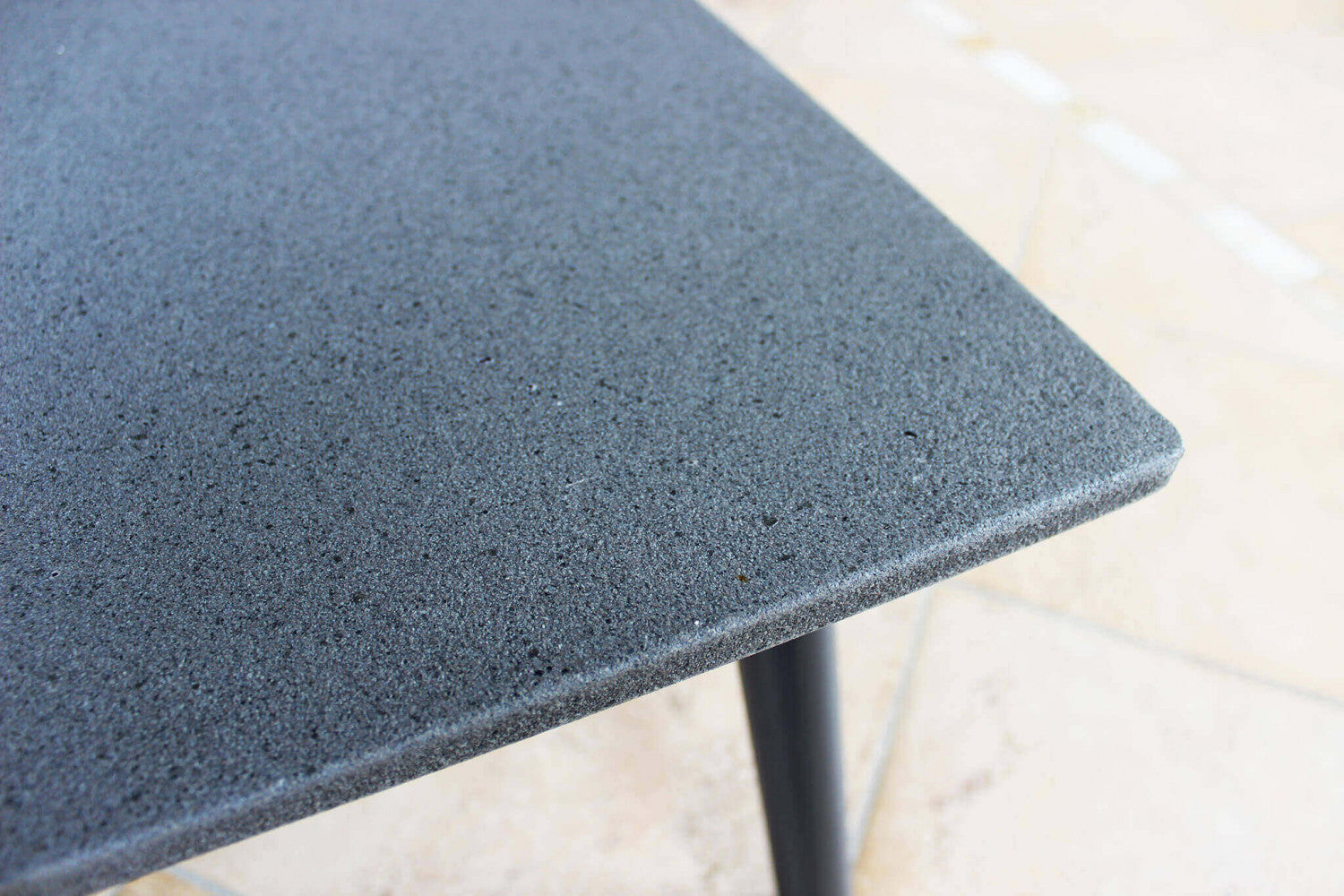 Dettaglio macro della superficie del tavolino in alluminio grigio, che rivela la finitura materica e la solidità del piano d'appoggio.