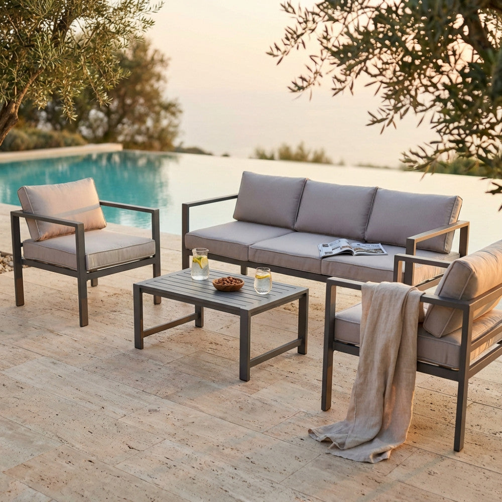 Vista angolare del set relax Avana in alluminio taupe con divano, due poltrone e tavolino su pavimentazione in travertino.
