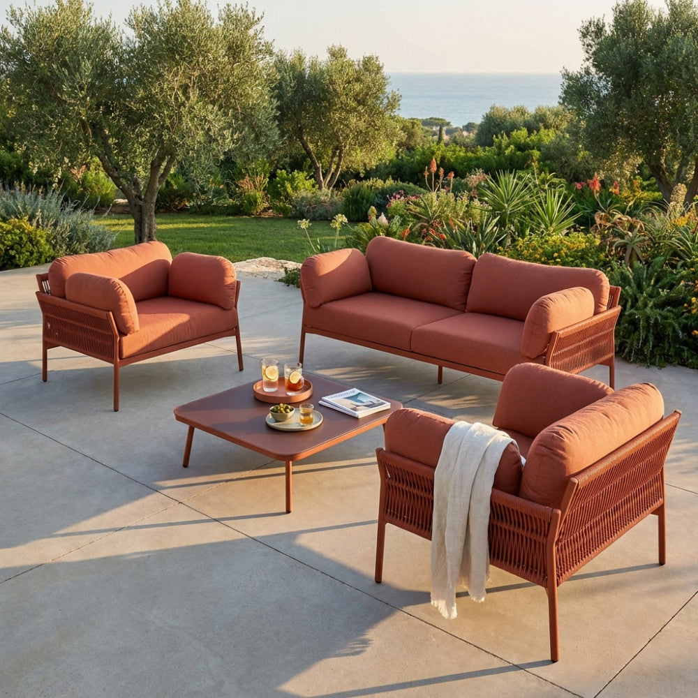 Il salotto da esterno Belém allestito su una terrazza soleggiata con vista su un giardino rigoglioso e sul mare.