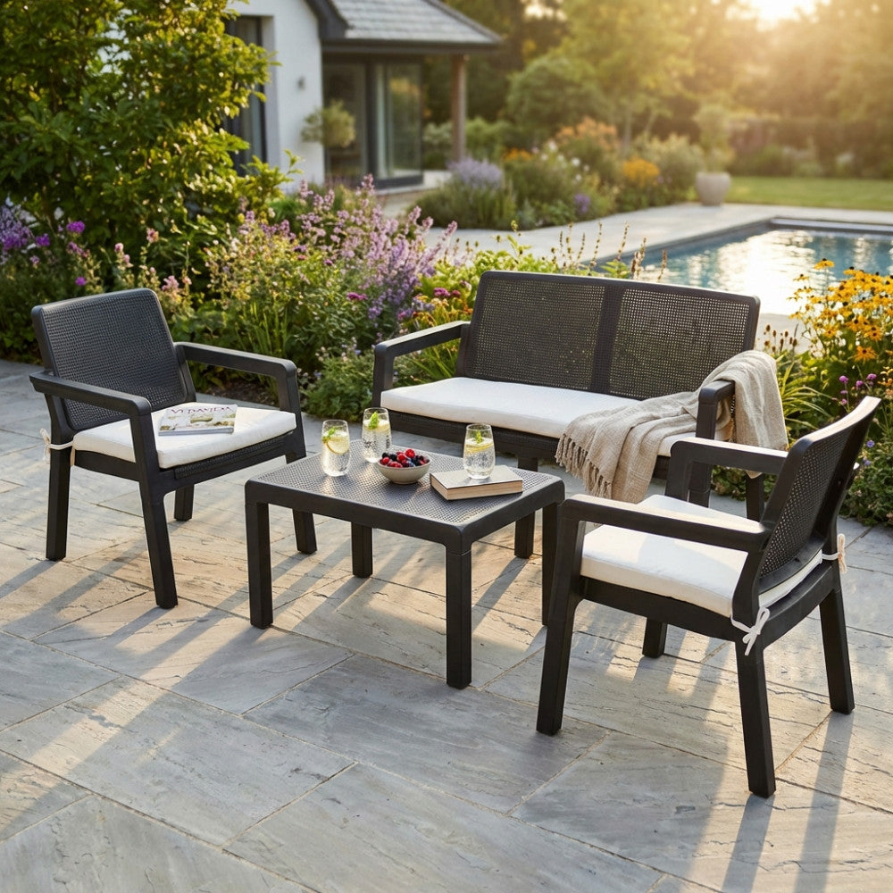 Set lounge Delaware con cuscini bianchi sfoderabili, ambientato in un rigoglioso giardino fiorito con piscina sullo sfondo.