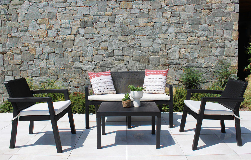 Salotto Delaware nero allestito su una terrazza con pavimentazione chiara e un muro in pietra grezza, arricchito da cuscini decorativi.