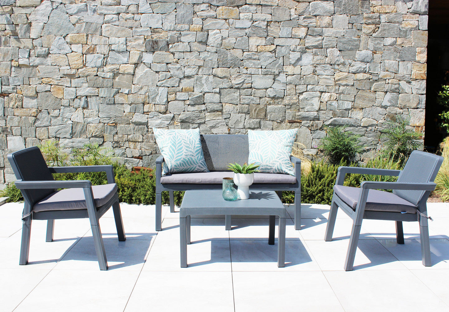 Salotto Delaware 2P in polipropilene grigio con cuscini grigi, in un ambiente esterno curato.