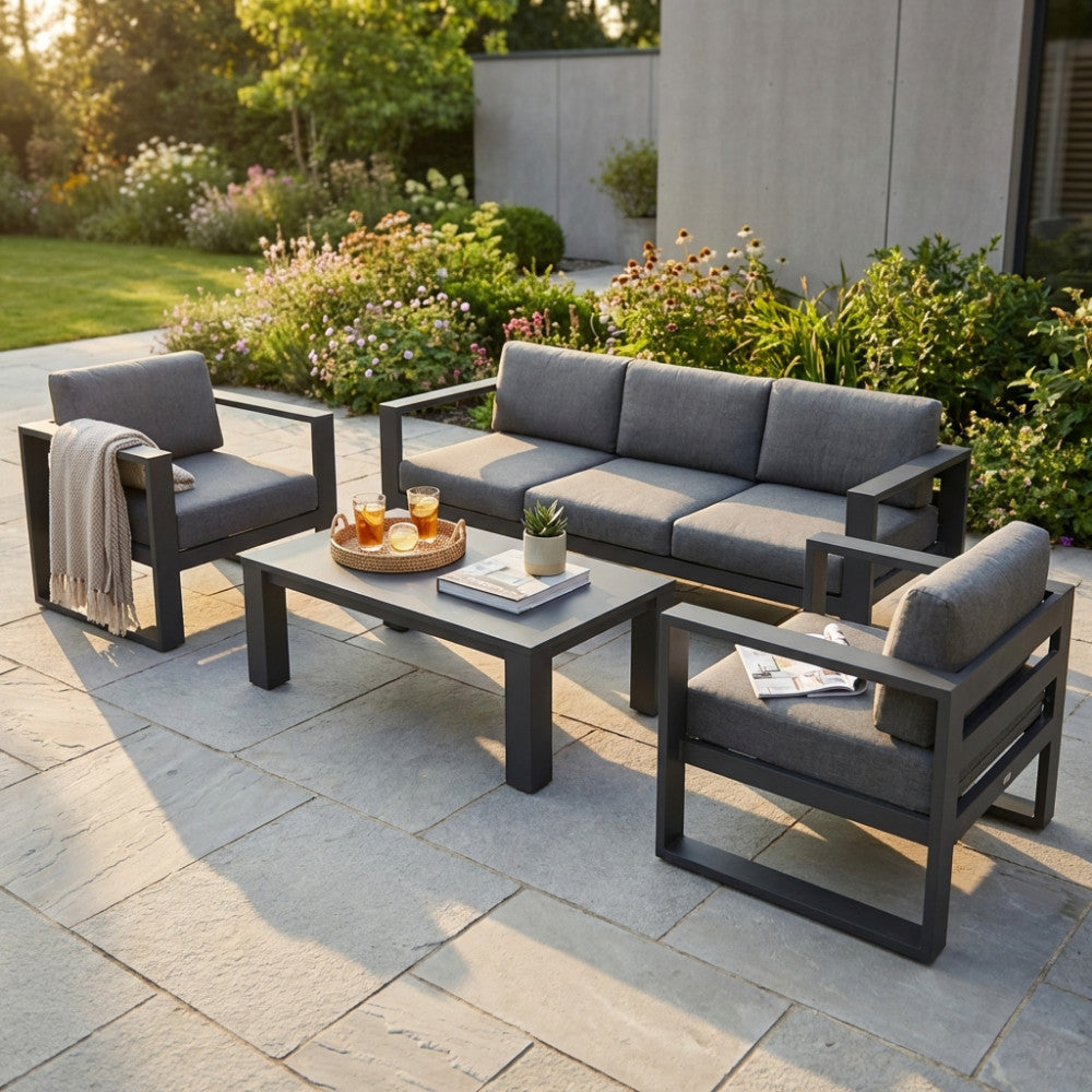 Set lounge Knoxville composto da divano a tre posti, due poltrone e tavolino in un giardino curato.