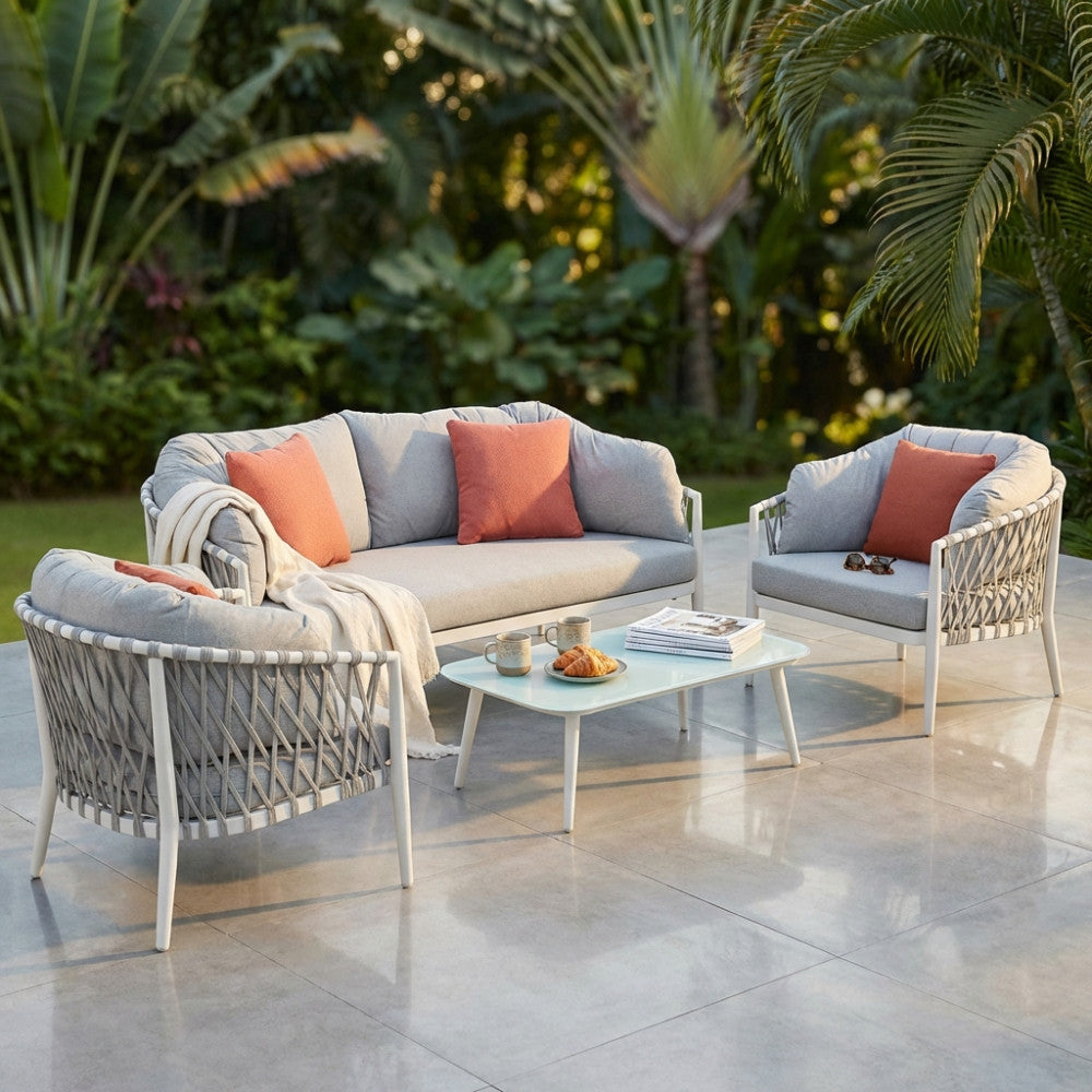 Salotto da esterno Mérida a 4 posti con struttura bianca, cuscini grigio chiaro e dettagli arancioni, ambientato su un patio tropicale.