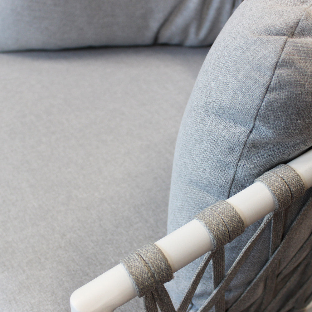 Particolare del bracciolo tubolare bianco con corda intrecciata e cuscino in misto cotone grigio chiaro.