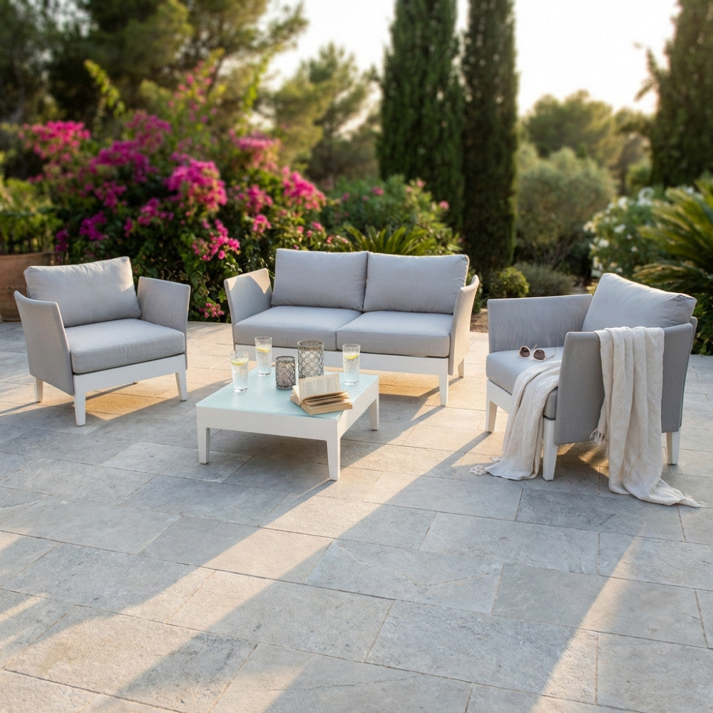 Salotto da esterno Minneapolis a 4 posti in alluminio bianco e textilene grigio, allestito su un patio in pietra naturale al tramonto.