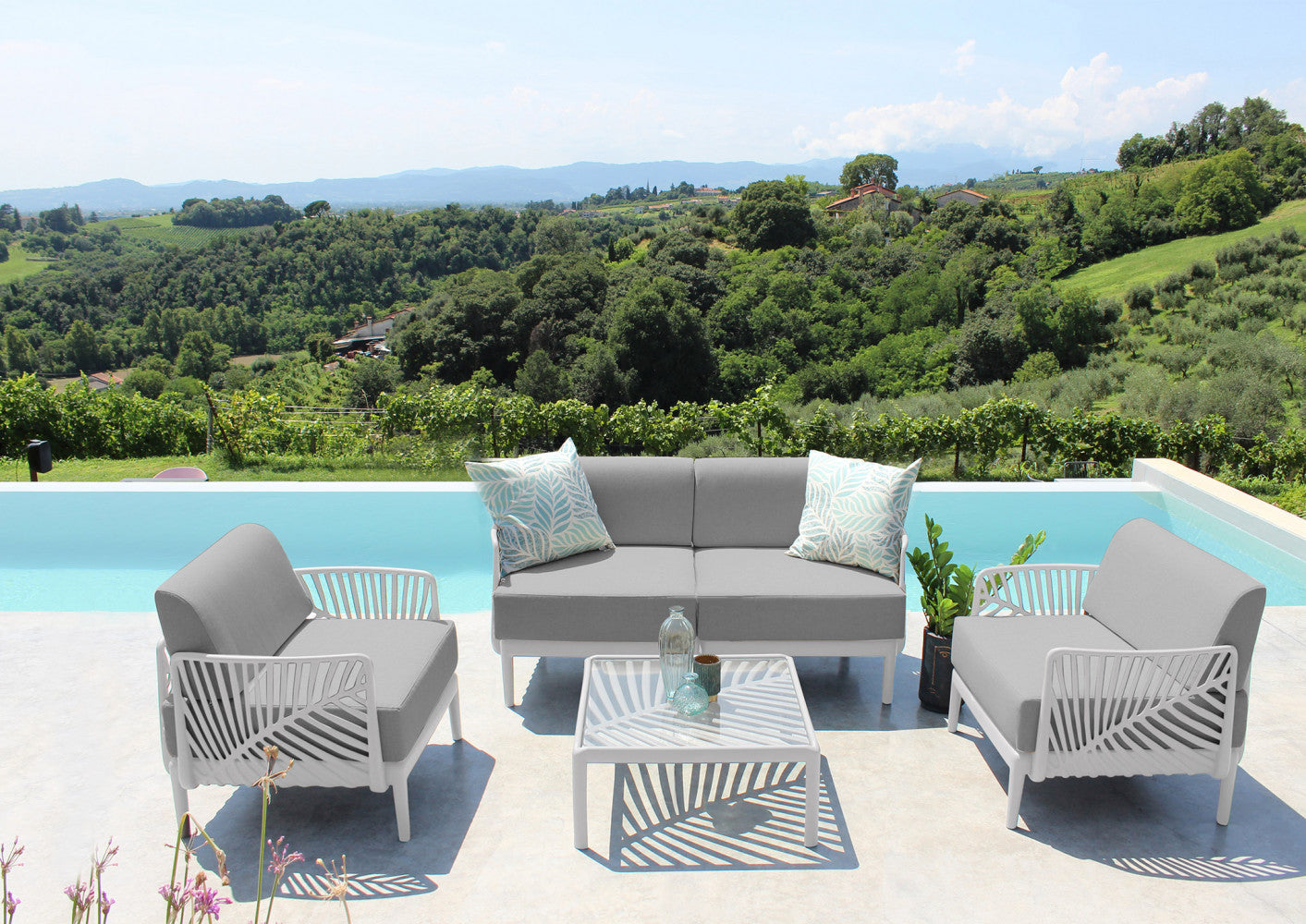 Set lounge Guaranà composto da divano a due posti e due poltrone con schienali in polipropilene bianco e cuscini grigi, posizionato su una terrazza panoramica con piscina.