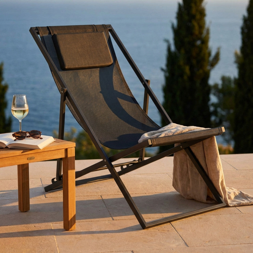 Sdraio Avana in acciaio e textilene antracite ambientata su una terrazza vista mare al tramonto con tavolino in teak.