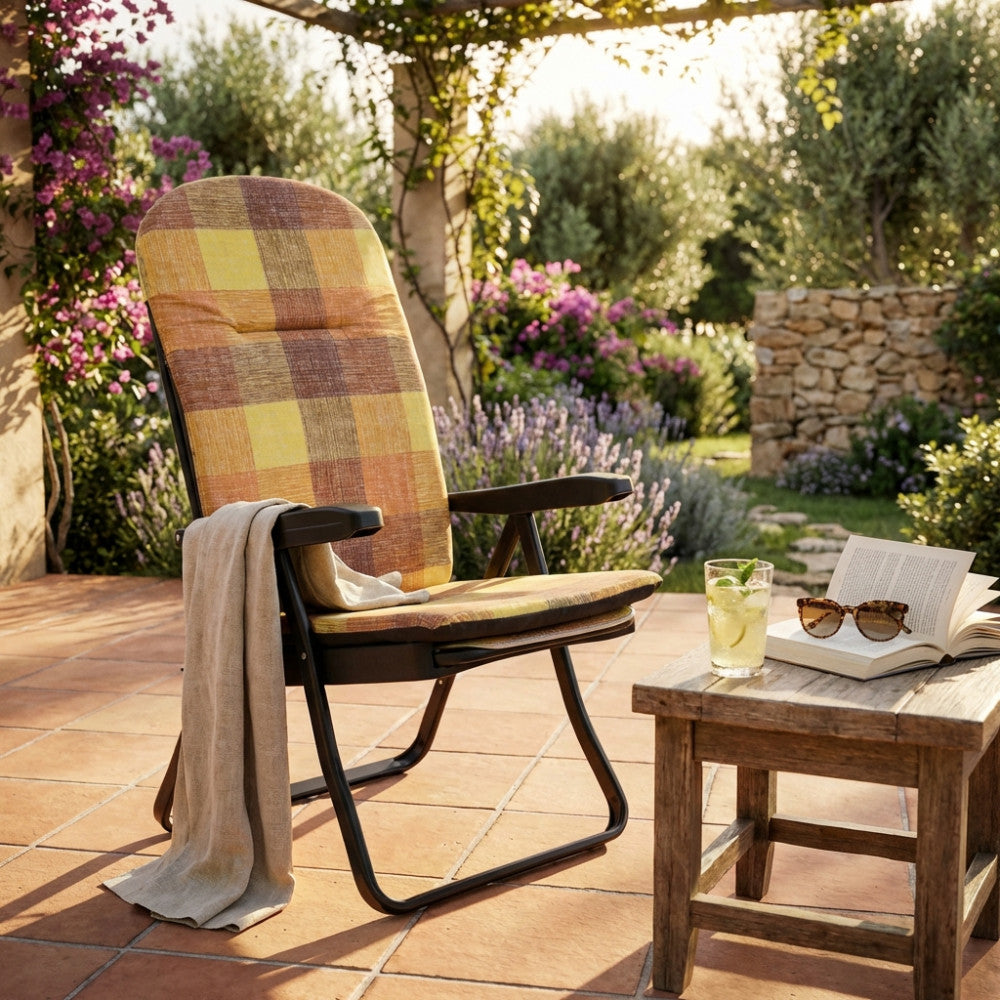Poltrona relax Cipro in tessuto a quadri arancio e giallo, ambientata su un patio in cotto con tavolino in legno e bibita fresca al tramonto.