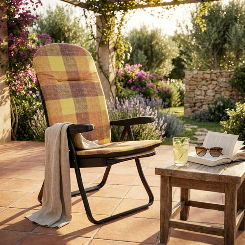 Poltrona relax Cipro in tessuto a quadri arancio e giallo, ambientata su un patio in cotto con tavolino in legno e bibita fresca al tramonto.