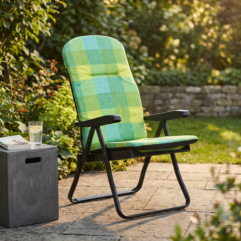 Poltrona relax Cipro in tessuto scozzese verde e giallo, ambientata in un giardino accanto a un tavolino in cemento.