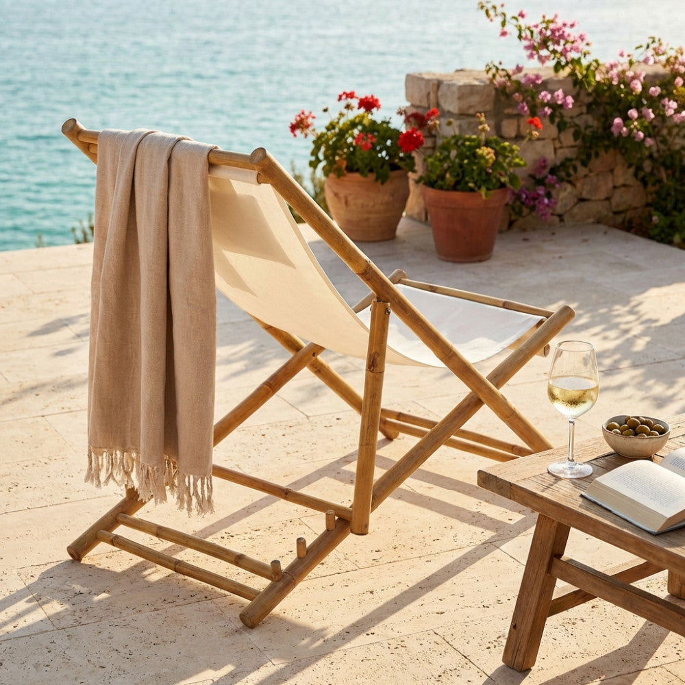 Sdraio dondolo Daiquiri in legno marrone con tessuto bianco, posizionata su una terrazza in pietra vista mare con asciugamano beige.