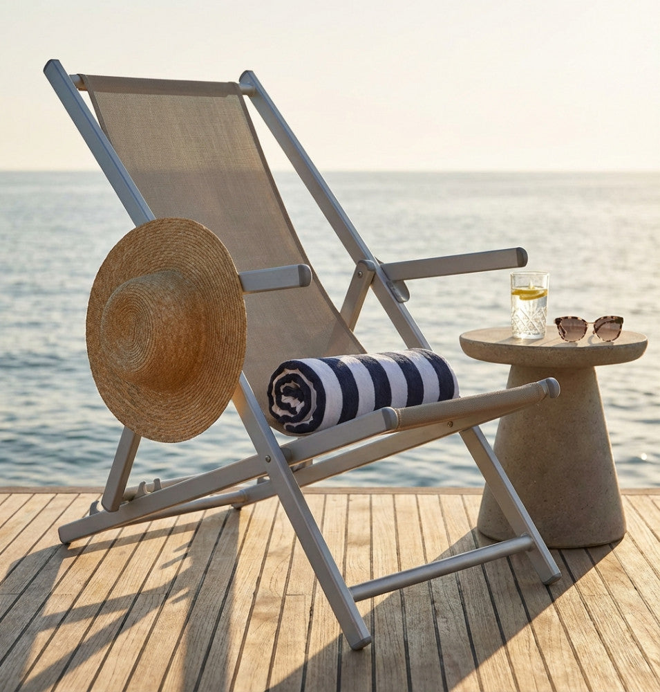 Sdraio BC807898-BEIG in alluminio e textilene tortora, ambientata su un molo in legno vista mare, con cappello di paglia e telo mare a righe.