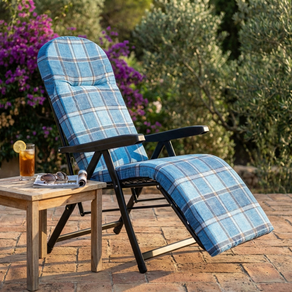 Vista laterale della poltrona relax in acciaio e tessuto tartan, affiancata da un tavolino in legno con bevanda rinfrescante.