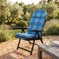 Poltrona relax Rodi in acciaio e tessuto scozzese blu ambientata in un giardino soleggiato su pavimentazione in cotto.
