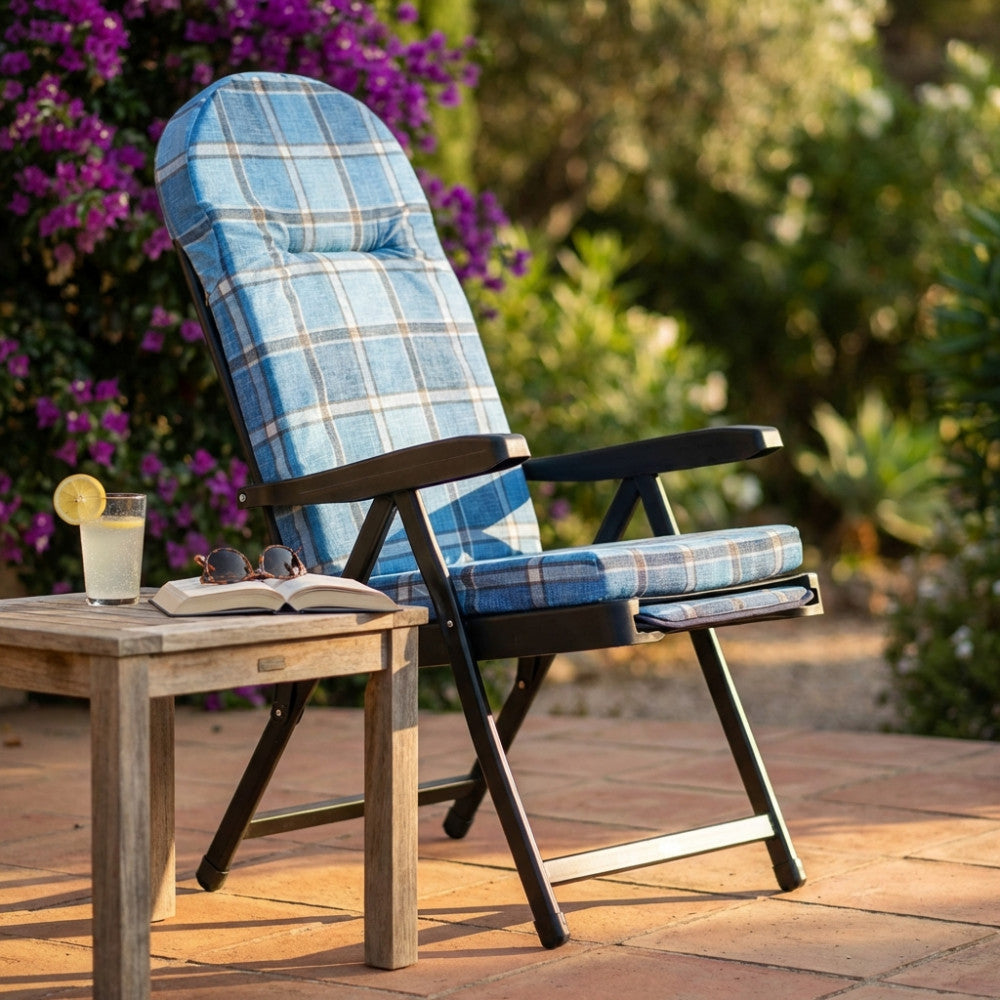 Vista laterale della poltrona relax Rodi con cuscino tartan azzurro, posizionata accanto a un tavolino in legno grezzo.