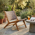 Poltrona lounge Alexander in teak massello posizionata su un patio in pietra accanto a un tavolino in cemento.